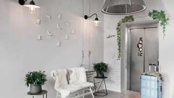 Un moderno vestíbulo con un sillón de piel blanca, dos plantas en macetas, una maleta azul e iluminación empotrada en la pared.
