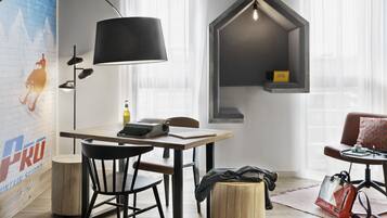 Una habitación moderna con una mesa de madera, una silla negra, una lámpara, un estante pequeño y un sofá.