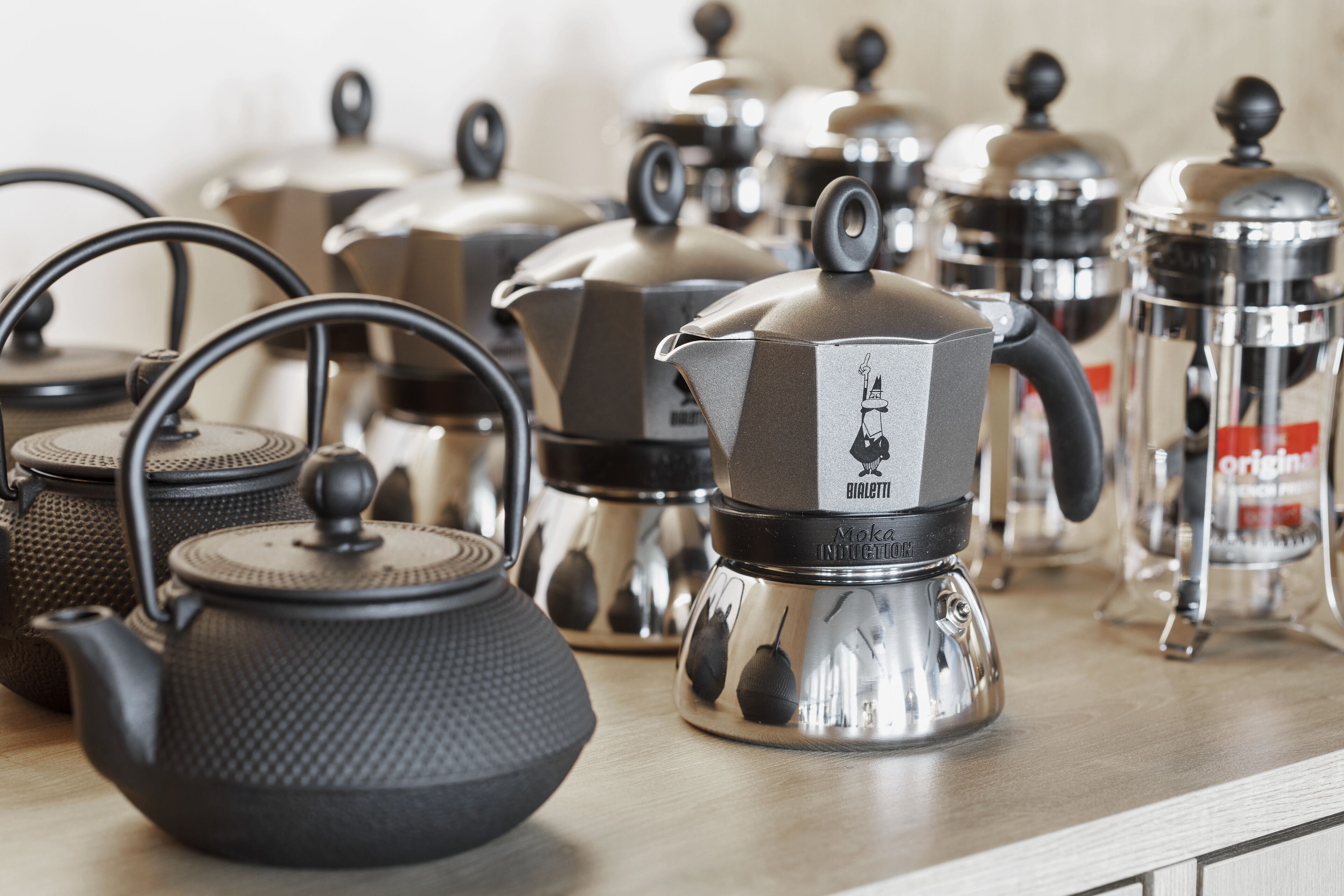 A kitchen with various tea kettles and coffee makers on the counter.