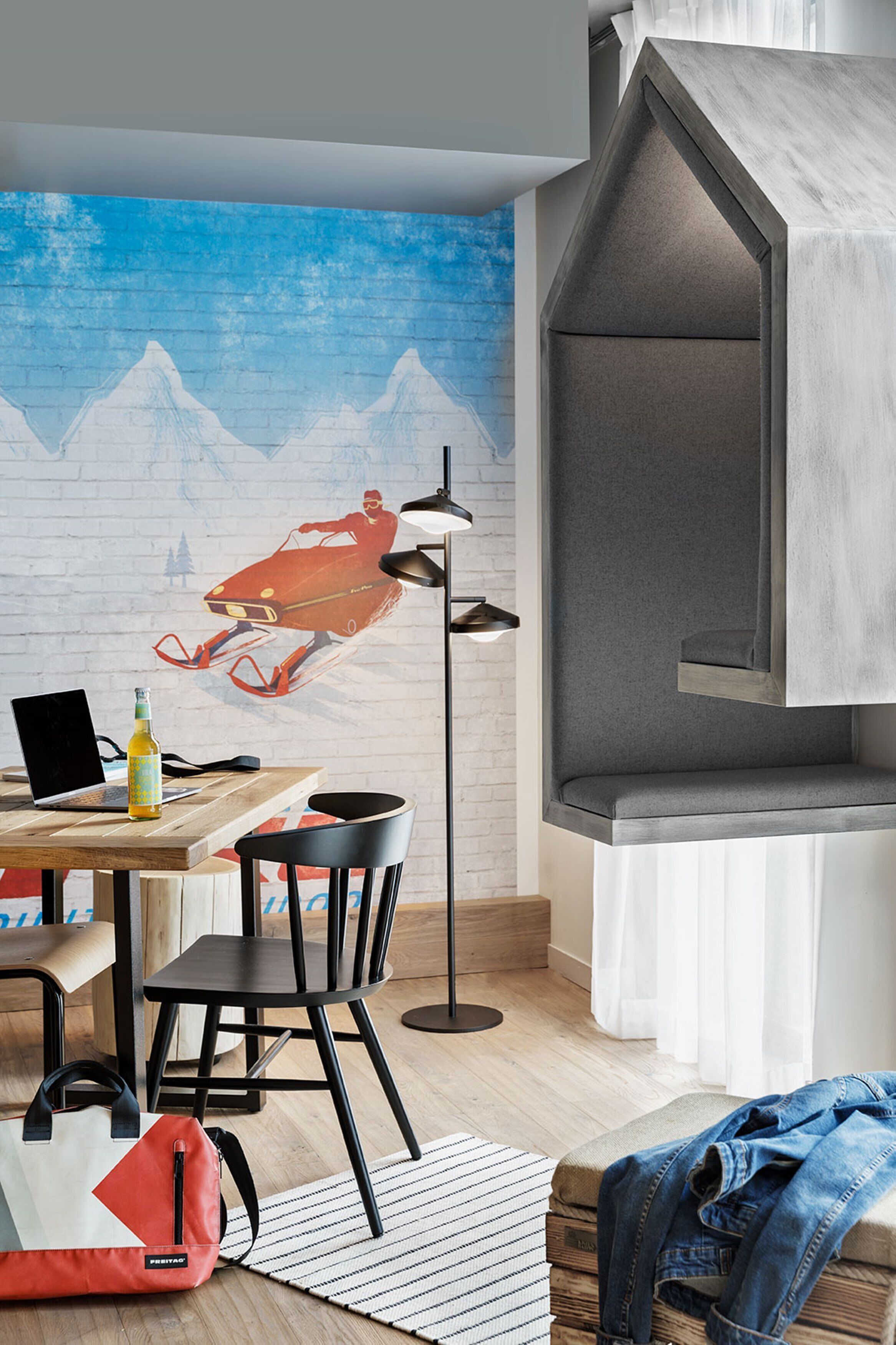 Una habitación moderna con un escritorio de madera, una silla negra, un bolso rojo y un mural con paisaje de montaña.