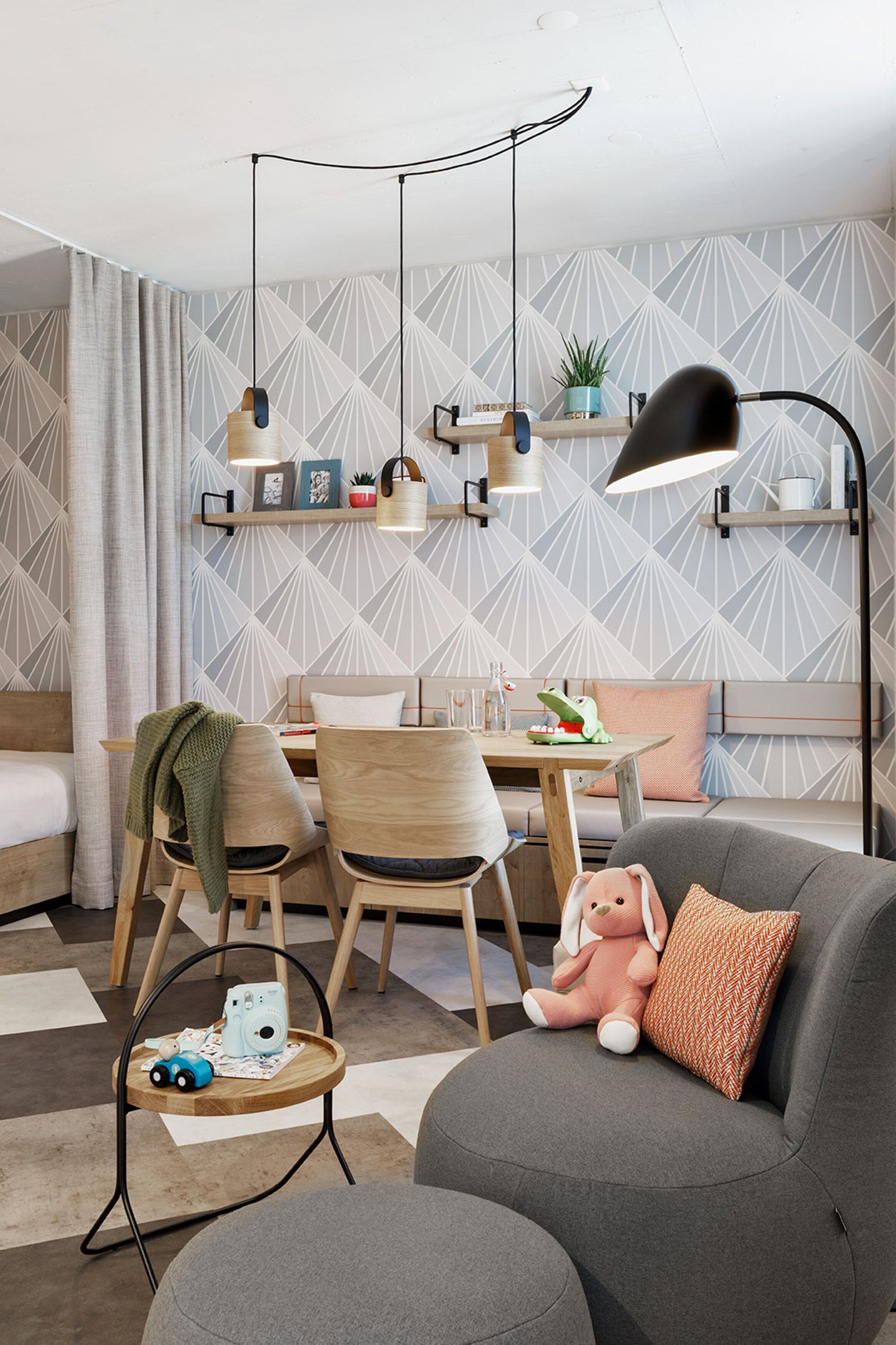 A modern living room with a sofa, a dining table, and chairs. There are shelves with decorative items and a hanging lamp.