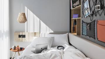 A neatly made bed with a laptop, a cup, and a small table with a bottle and a cup.