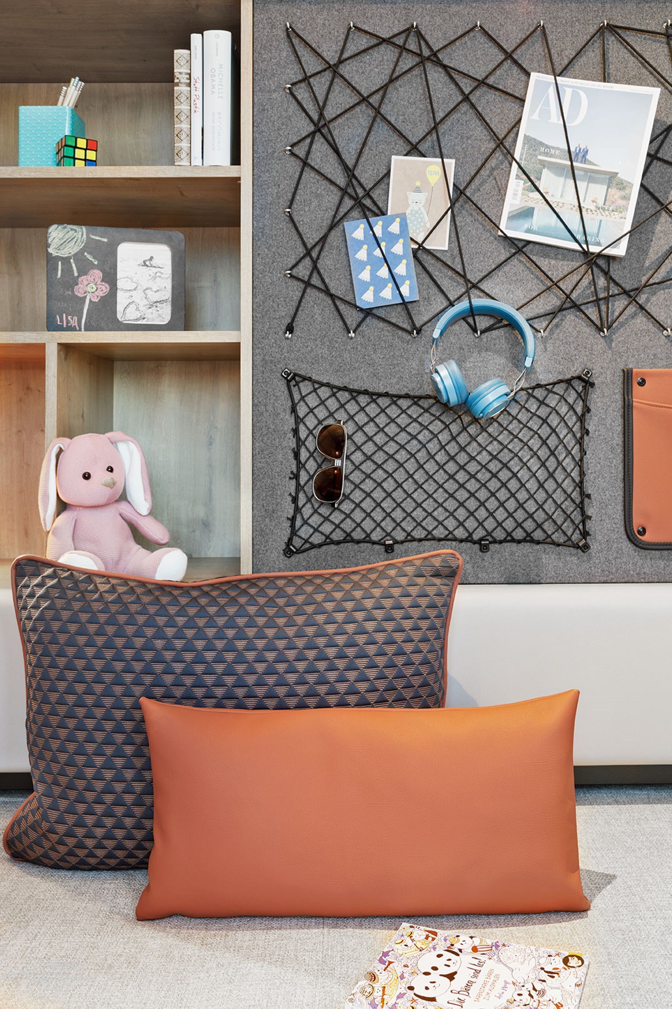 A room with a bookshelf, a wall-mounted geometric decoration, and two patterned pillows.