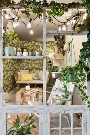 A cozy, well-lit room with a sofa, a chair, and a table, decorated with plants and string lights. - Stay KooooK Bern Wankdorf – Online Check In (Bern)