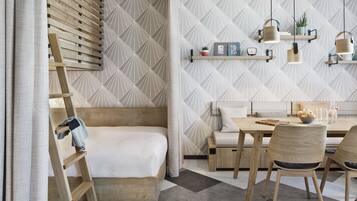 Une chambre moderne avec un lit en mezzanine, un coin repas comprenant une table et des chaises, et un mur recouvert d’un papier peint à motifs géométriques.