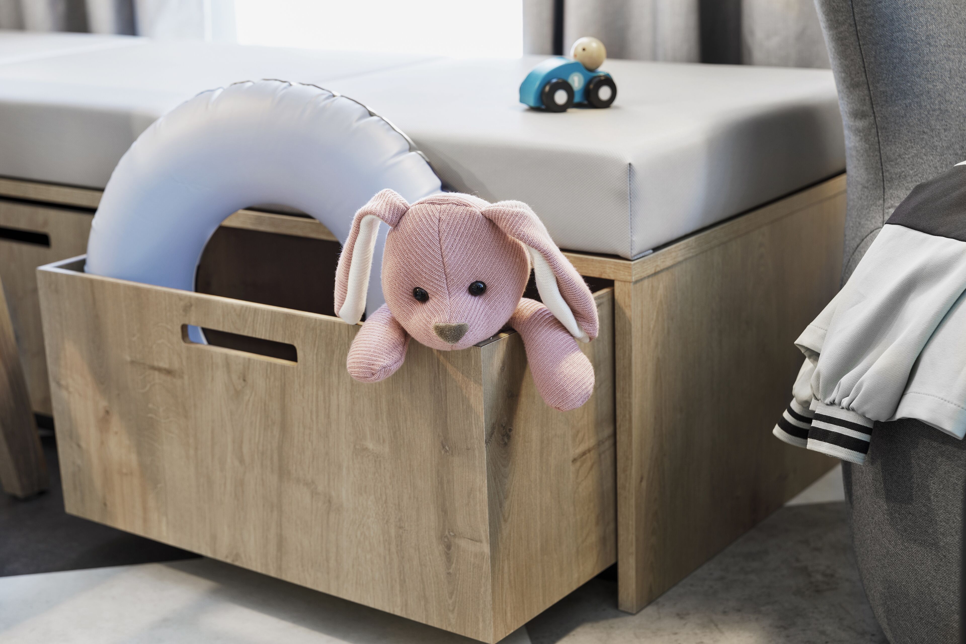 A wooden storage box with a plush toy and a blue toy car on top.