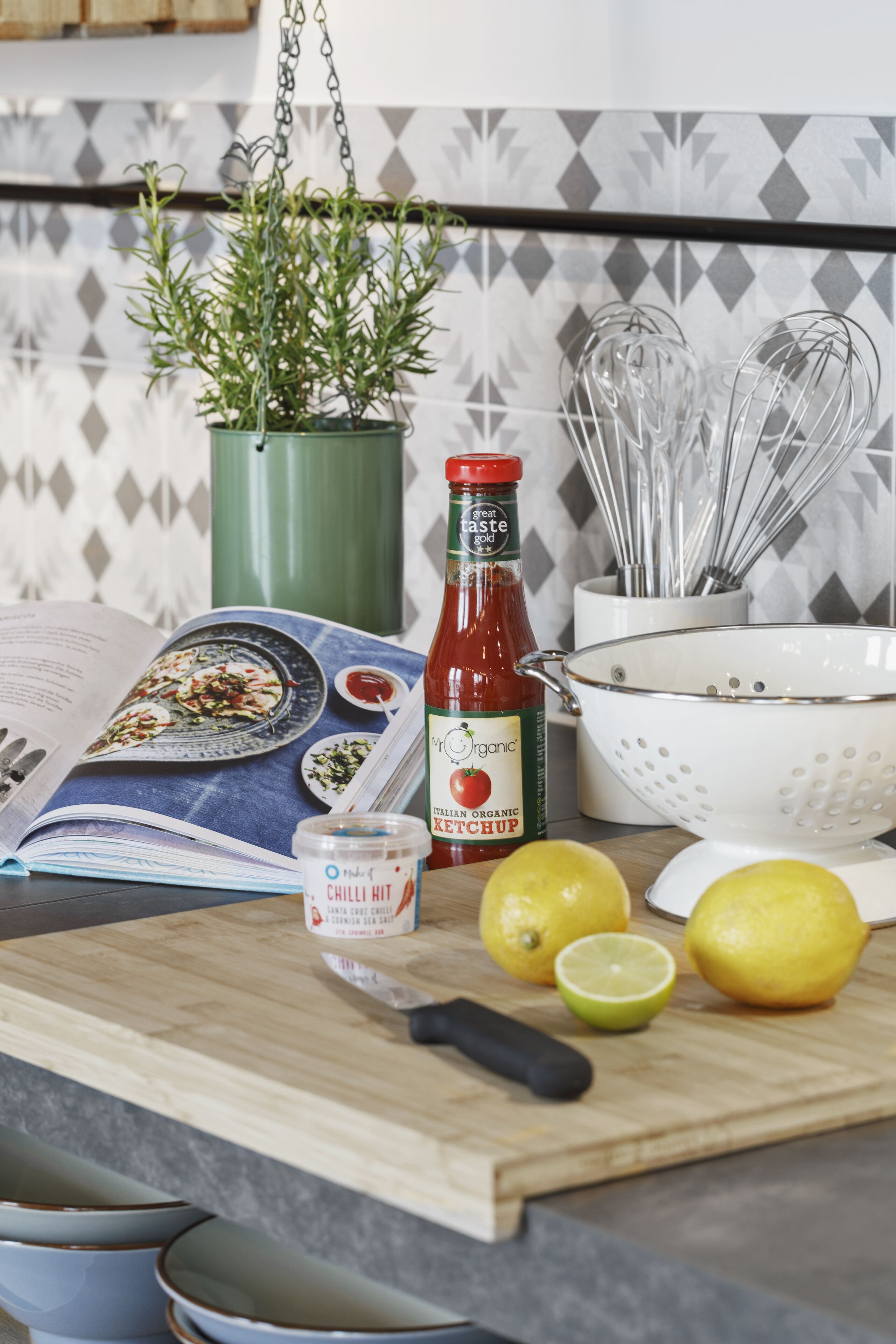 Eine Küchenarbeitsplatte mit Schneidebrett, einem Buch, einer Ketchup-Flasche, Zitronen und Küchenutensilien.