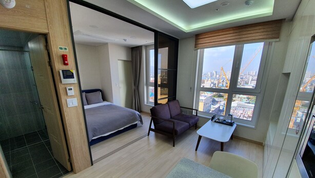 Ein modernes Hotelzimmer mit Bett, Sofa, Esstisch und Blick auf die Stadt.