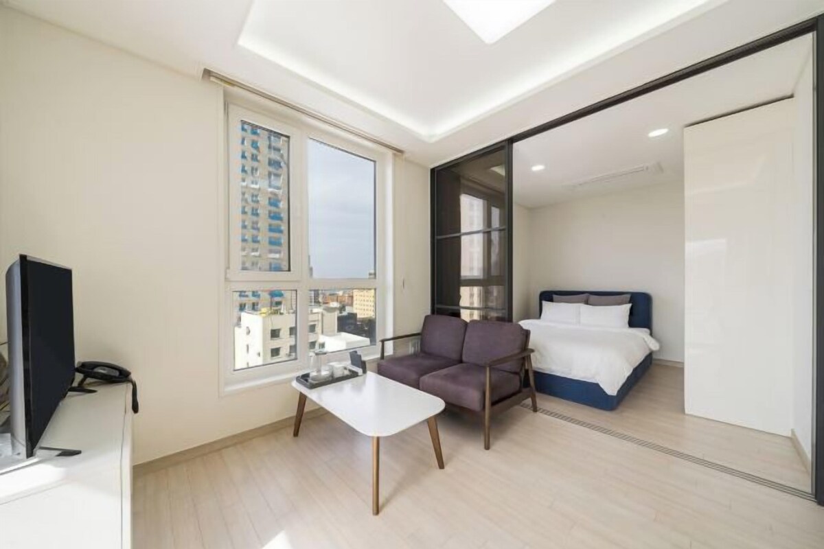 A modern hotel room with a bed, a sofa, a small table, and a TV.