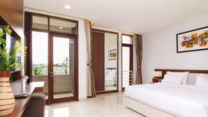 A modern hotel room with a large bed, a desk with a computer, a potted plant, and a sliding glass door leading to a balcony. - Rozelle Hotel (Bandung)