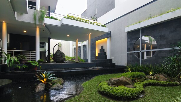 A modern building with a central courtyard featuring a water feature, potted plants, and a stone pathway. - Rozelle Hotel (Bandung)