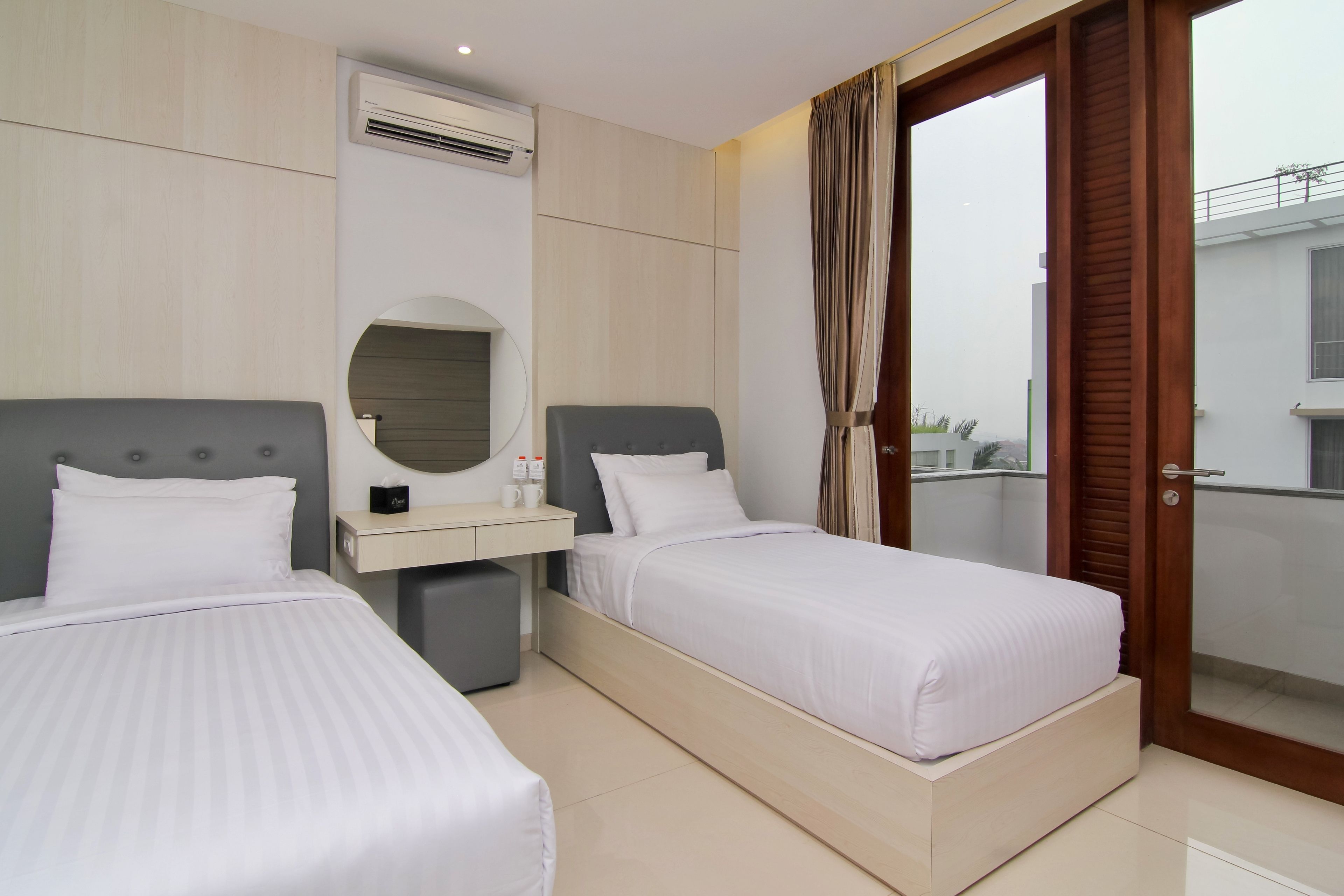 A hotel room with two beds, a bedside table, a mirror, and an air conditioning unit.