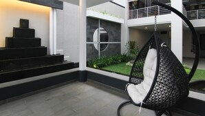 A modern interior with a hanging chair, a staircase, and a view of a garden. - Rozelle Hotel (Bandung)