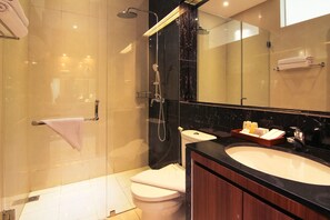 A modern bathroom with a glass-enclosed shower, a toilet, a sink with toiletries, and a large mirror.