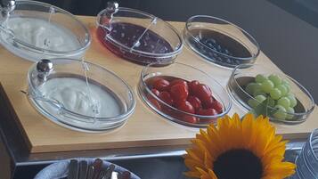 Un bufé con diferentes alimentos, entre ellos yogur, tomates cherry, uvas y un girasol.