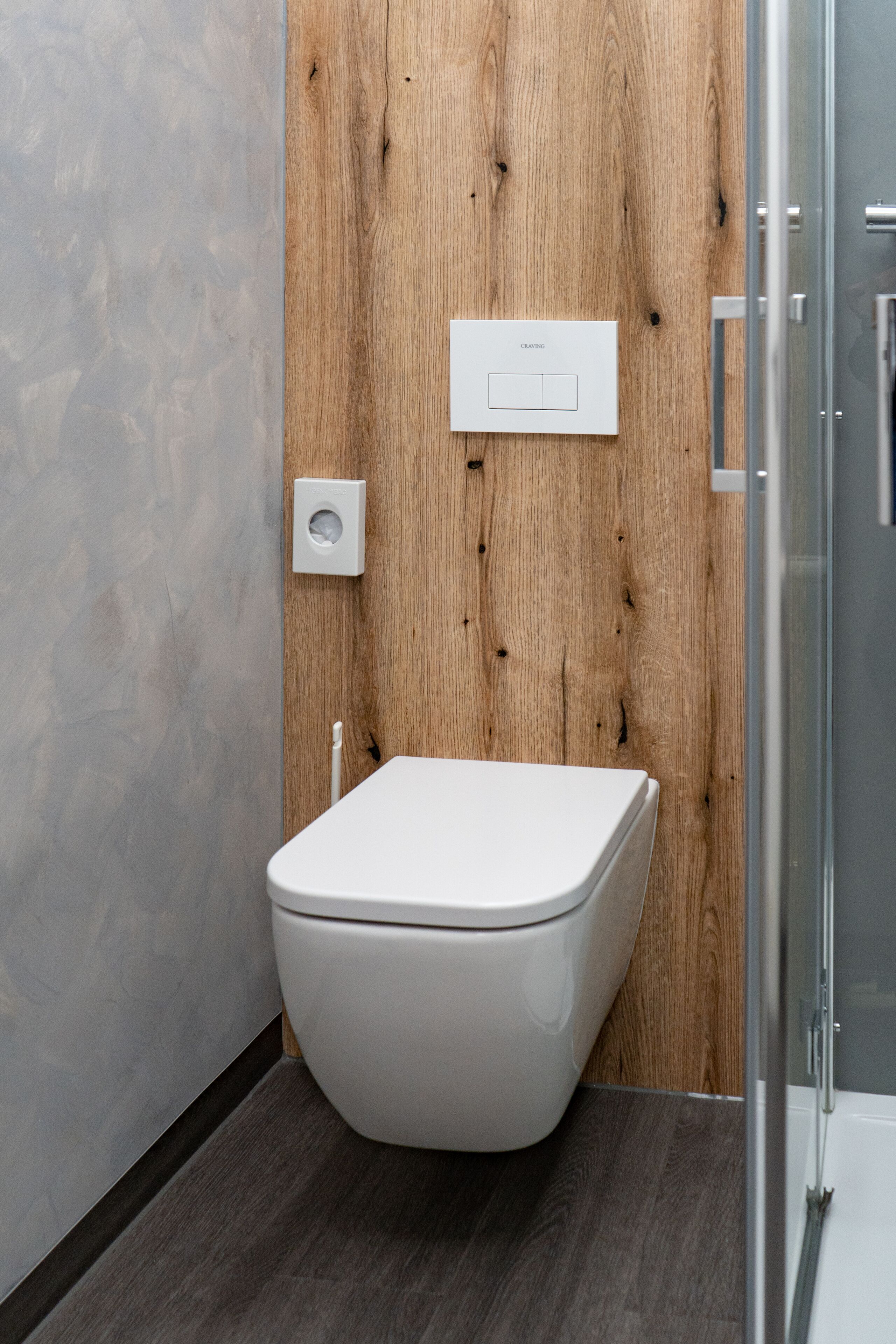 A modern bathroom with a wooden panel wall, a white toilet, and a glass shower enclosure.