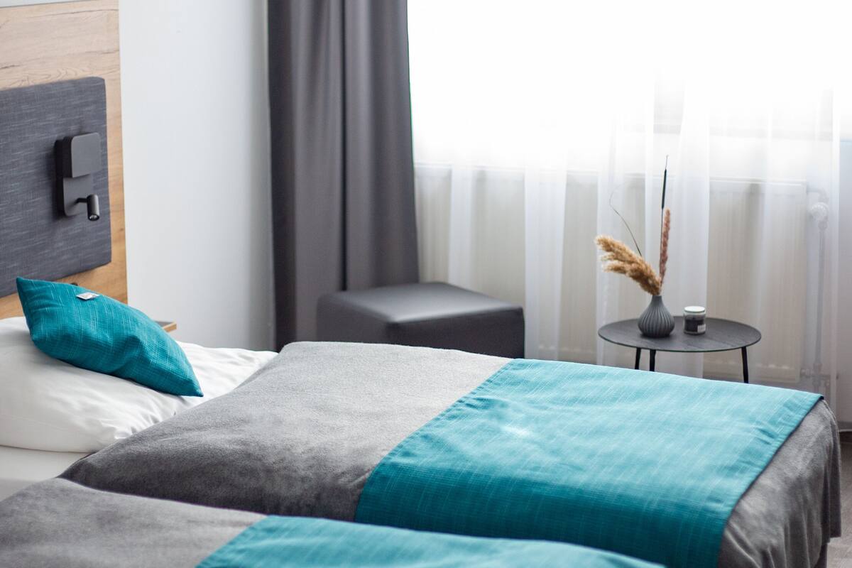 A hotel room with two beds, a small table with a vase, and a chair.