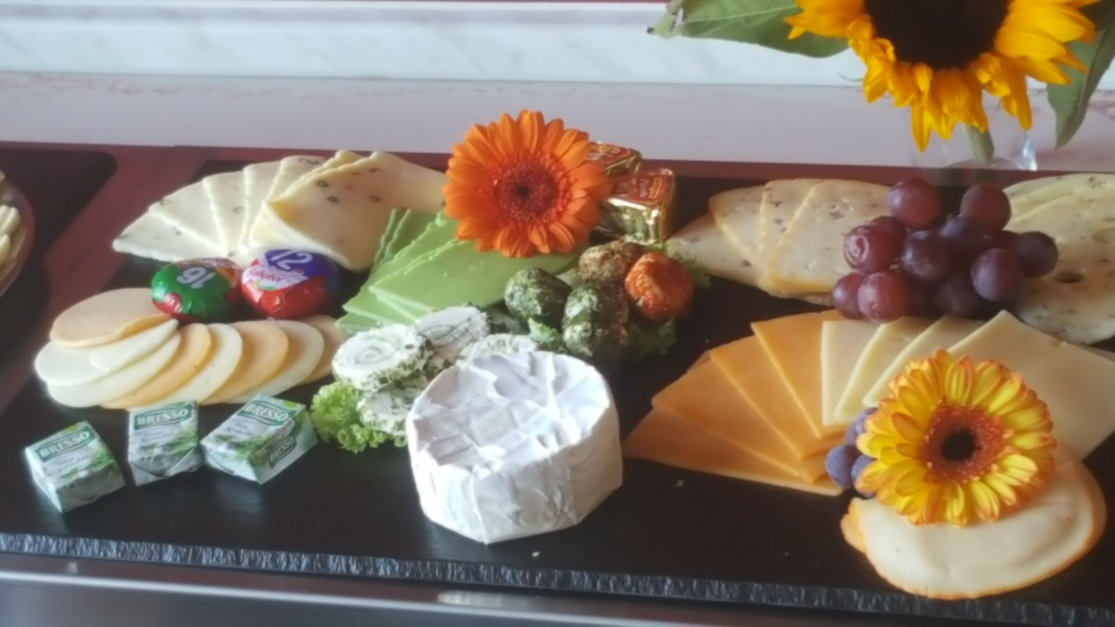 A cheese board with various cheeses, grapes, and decorative flowers.