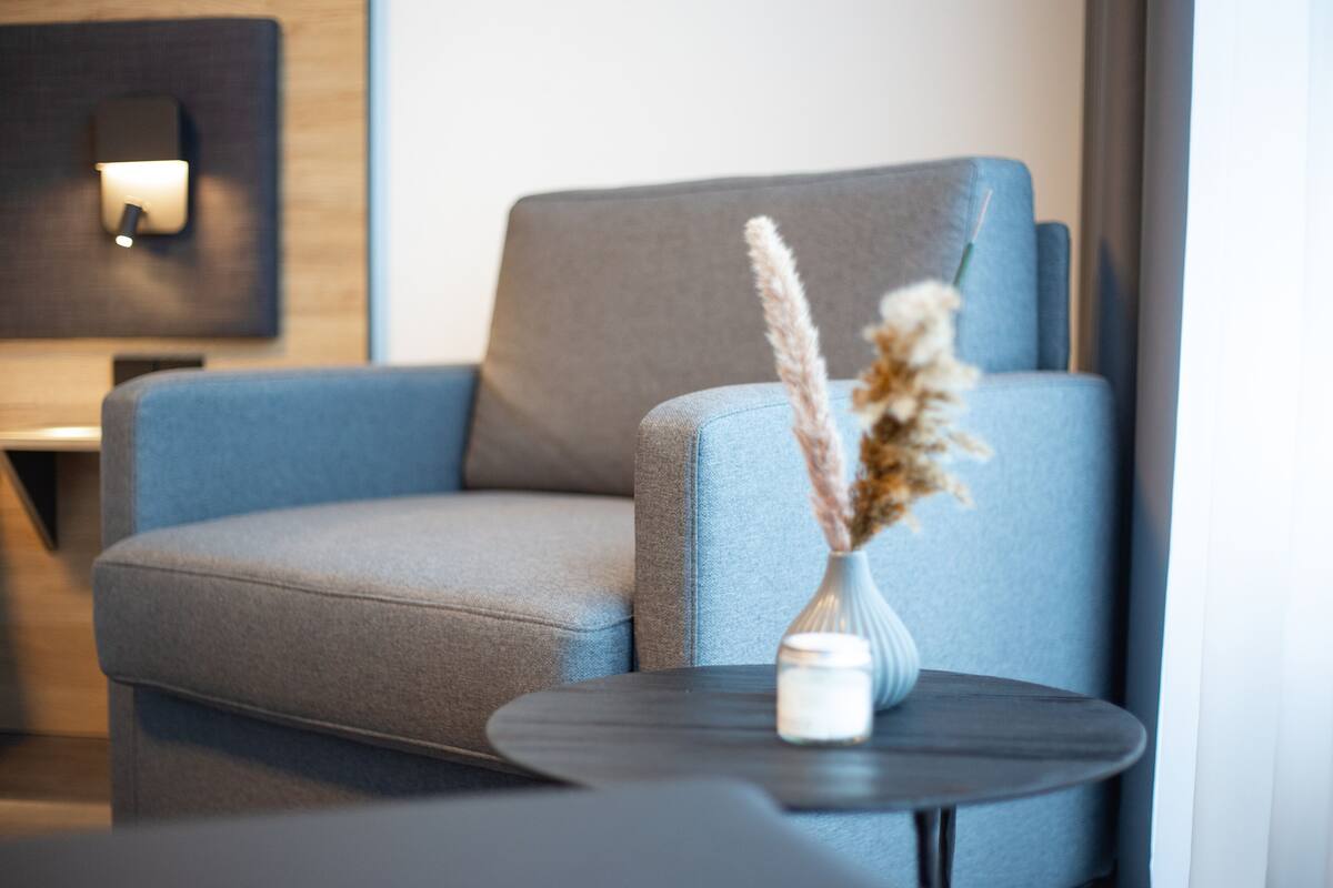 A modern living room with a grey sofa, a small round table, and a vase with dried flowers.