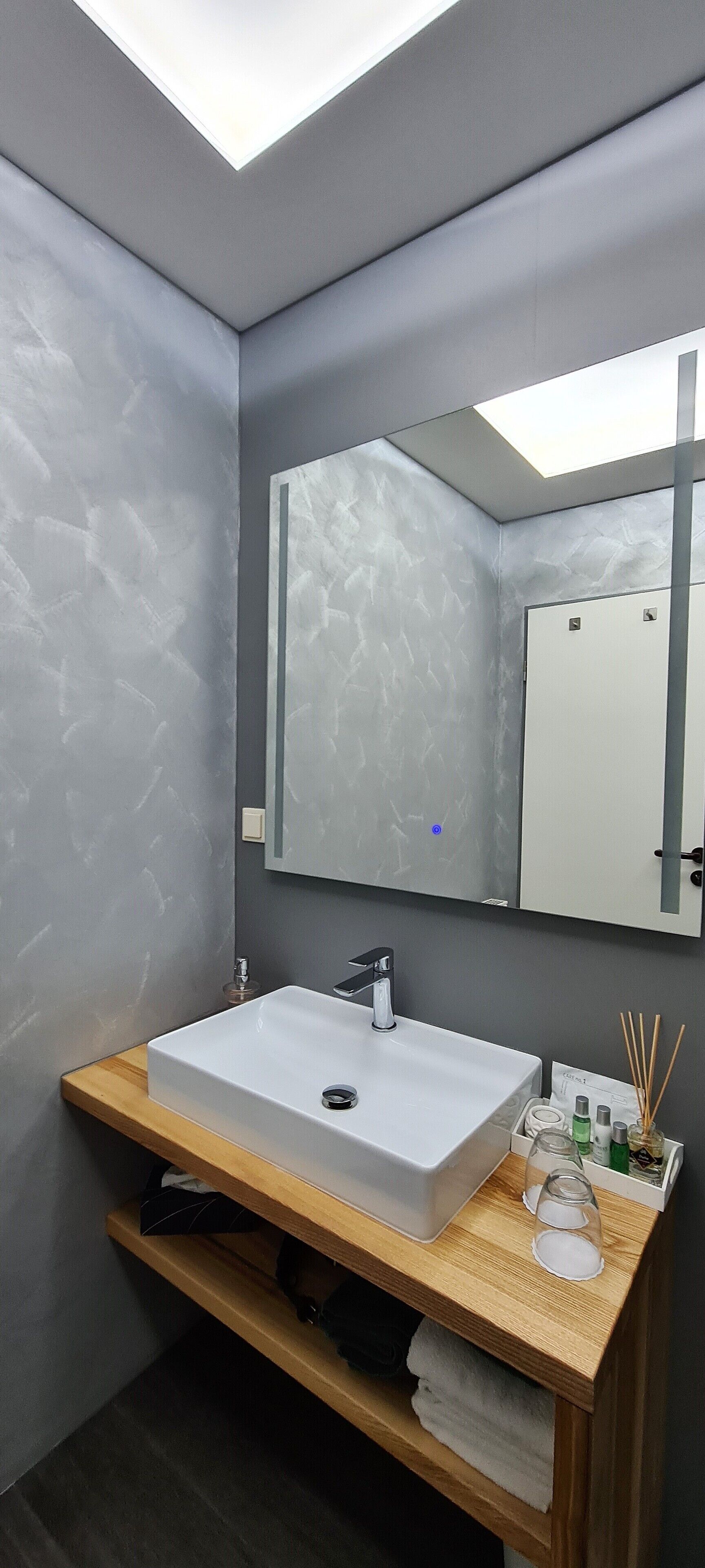 A modern bathroom with a white sink, a mirror, and a wooden vanity.