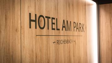Eine Holzverkleidung mit der Aufschrift 'HOTEL AM PARK' und 'REICHENBACH', welche den Namen und den Standort des Hotels angibt.
