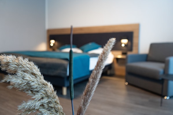 A modern hotel room with a bed, a sofa, and a nightstand with a lamp. - Hotel Am Park (Reichenbach im Vogtland)