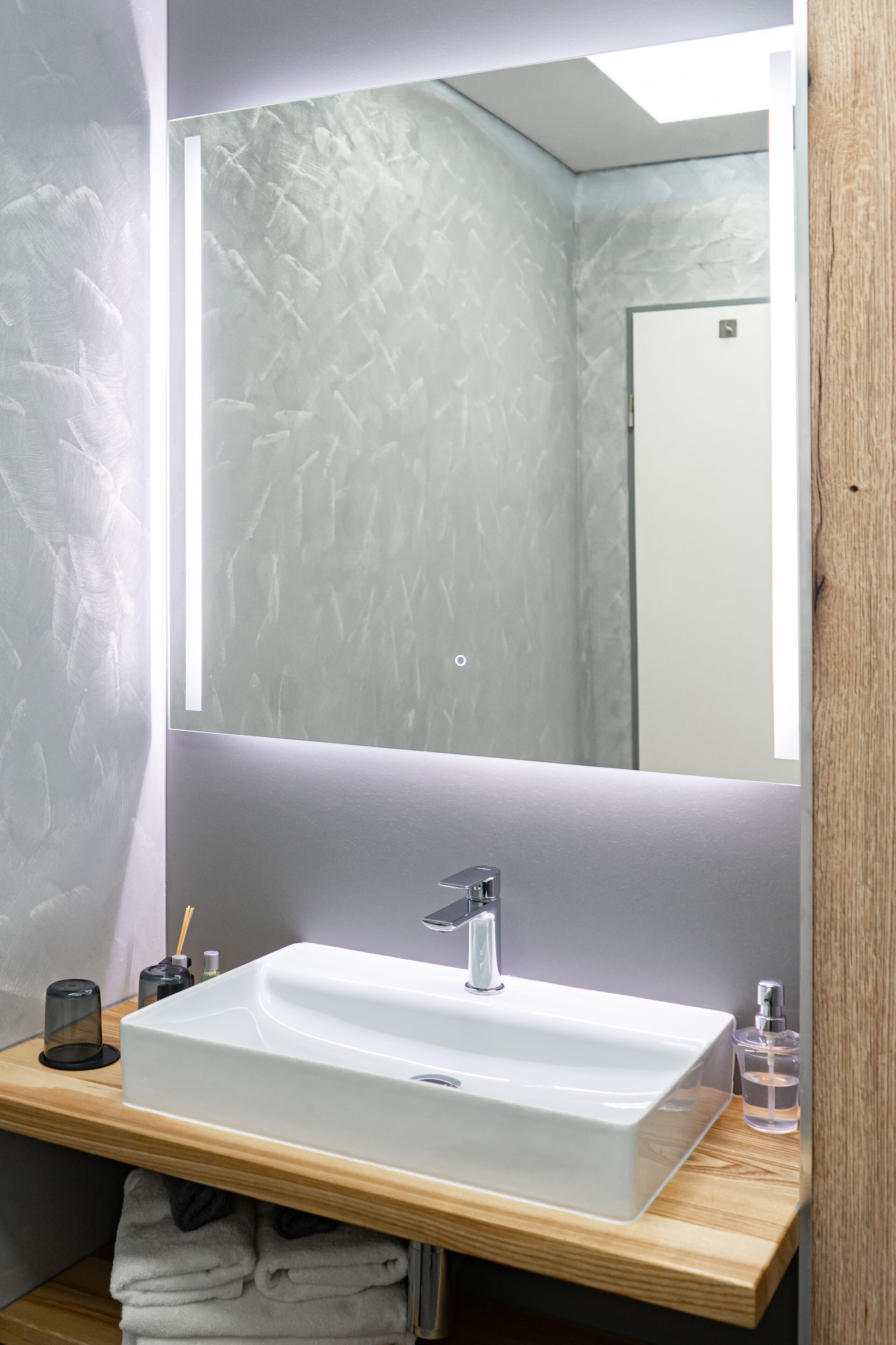A modern bathroom with a rectangular white sink, a large mirror, and a wooden countertop.
