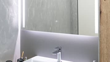 A modern bathroom with a rectangular white sink, a large mirror, and a wooden countertop.