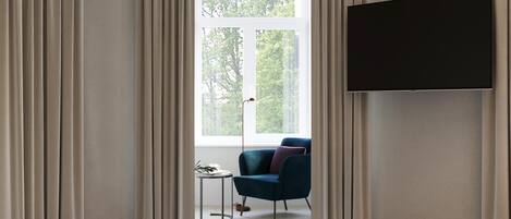 A bedroom with a bed, a TV, a chair, and a window with curtains.