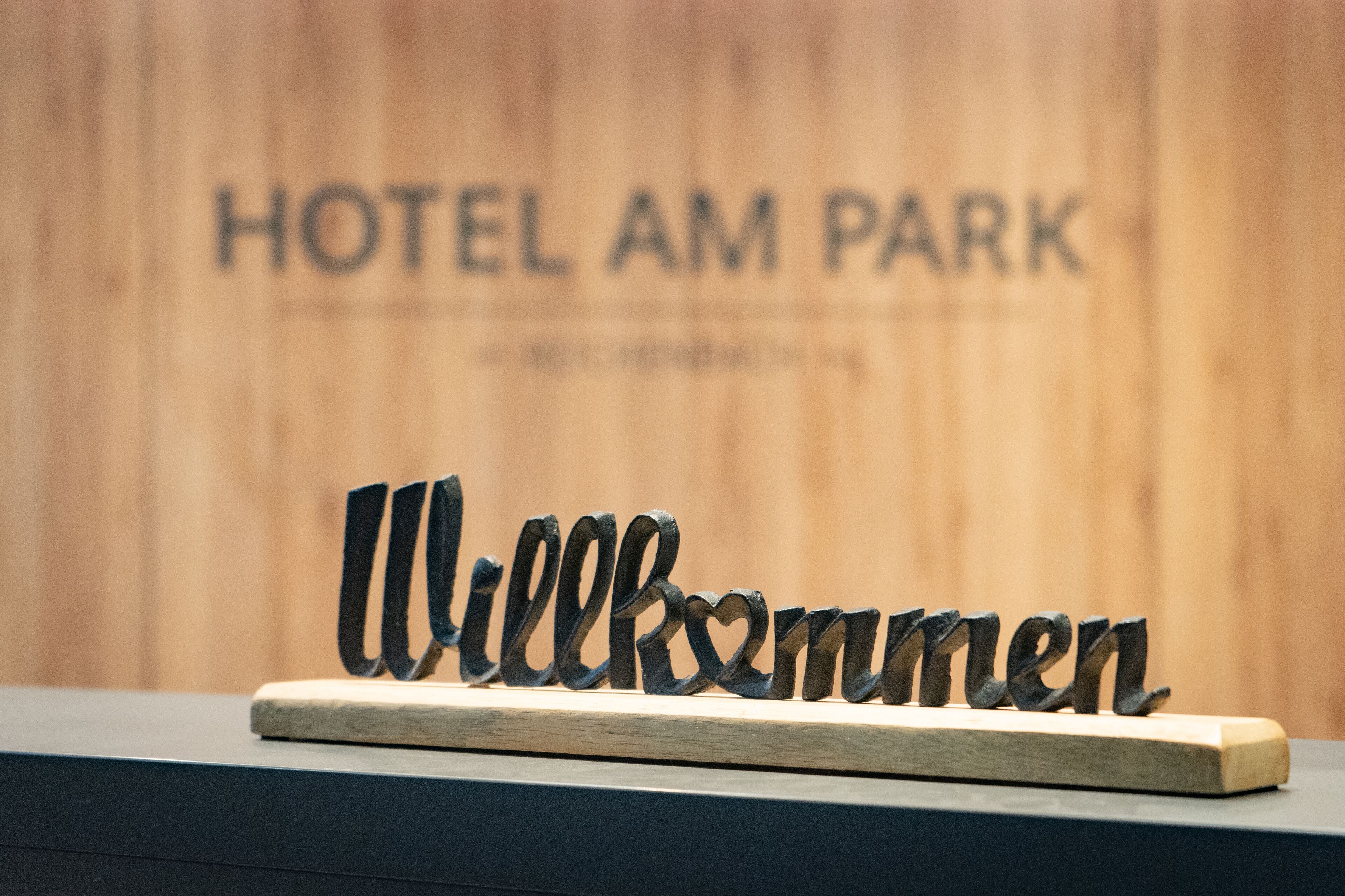 A welcome sign with the text "Willkommen" in front of a wooden wall with "HOTEL AM PARK" written on it.