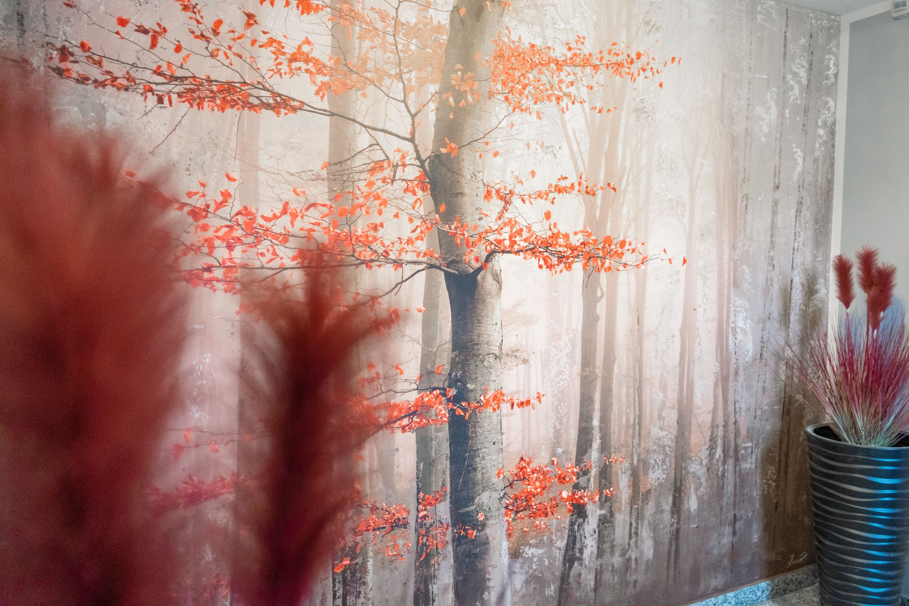 A room with a wooden wall, a large tree painting, and a tall vase with red foliage.