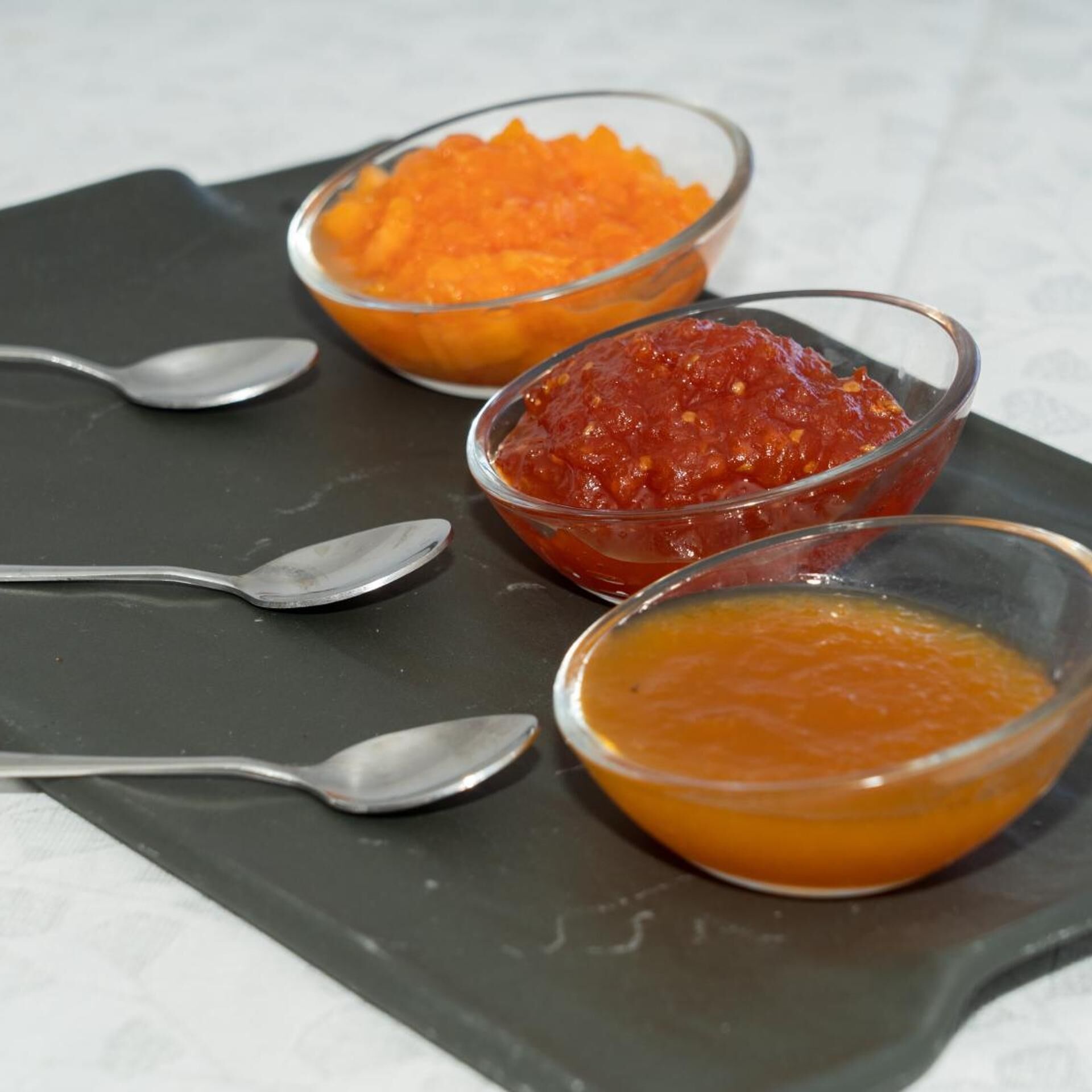 Tres tazones de comida sobre una tabla de pizarra oscura con cucharas.