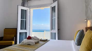 A hotel room with a bed, a chair, and a view of the sea.