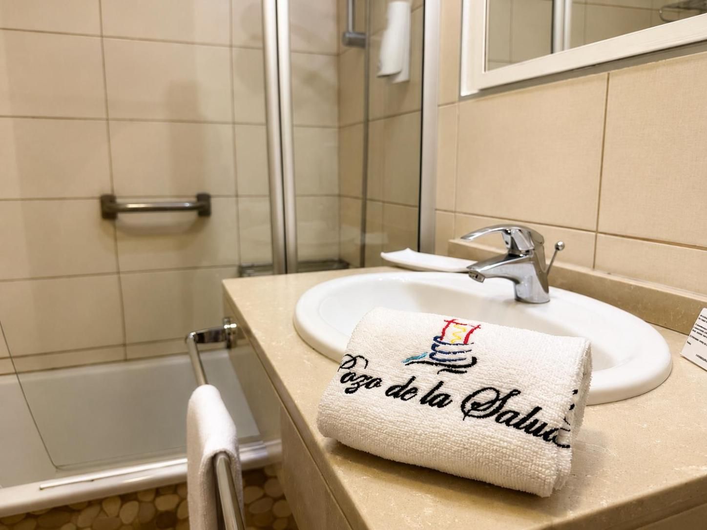 Un baño con un lavamanos blanco, una toalla con texto y una zona de ducha.