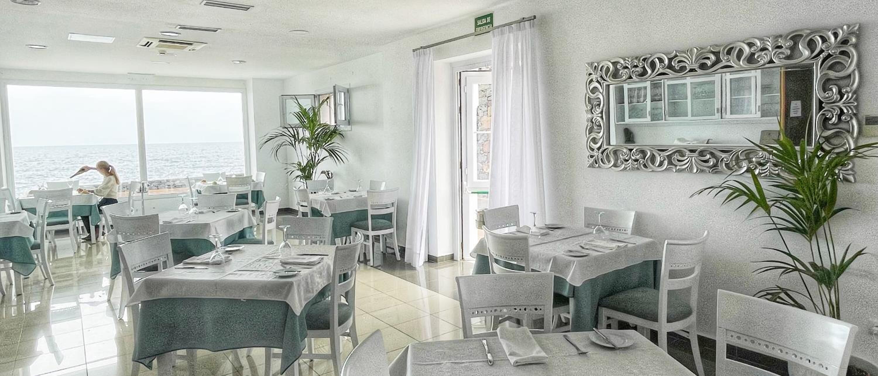 Un restaurante con mesas y sillas, un espejo grande y vista al mar.