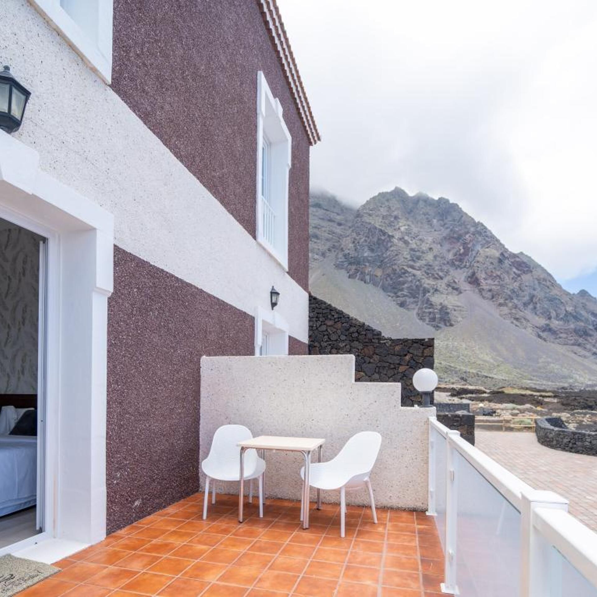 A terrace with a table and chairs, a stone wall, and a mountain view.