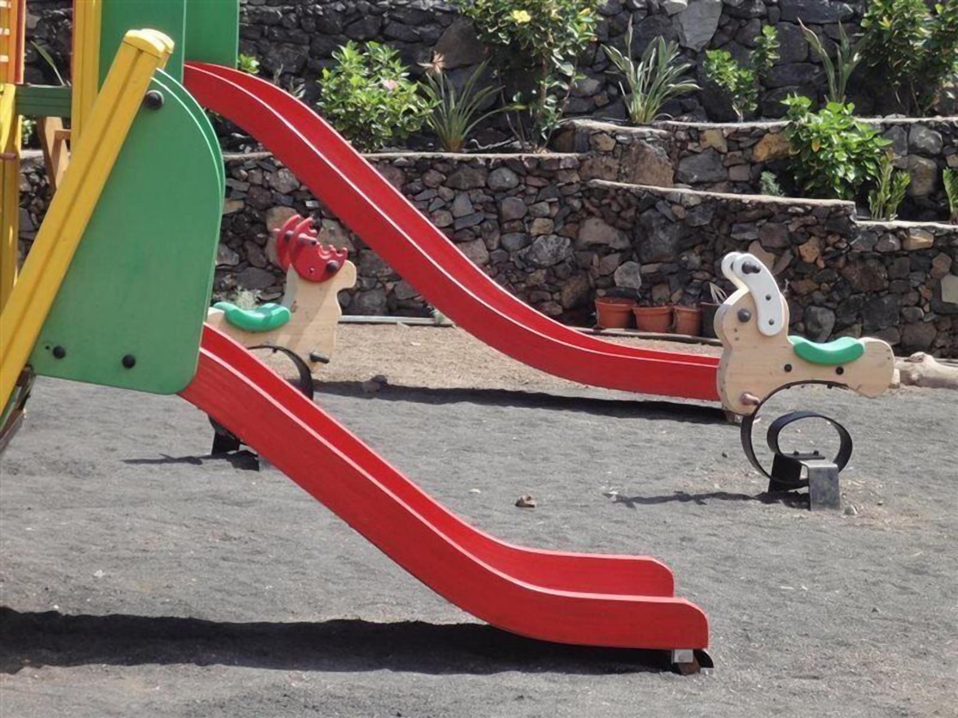 Une aire de jeux avec un toboggan rouge et une structure d’escalade.