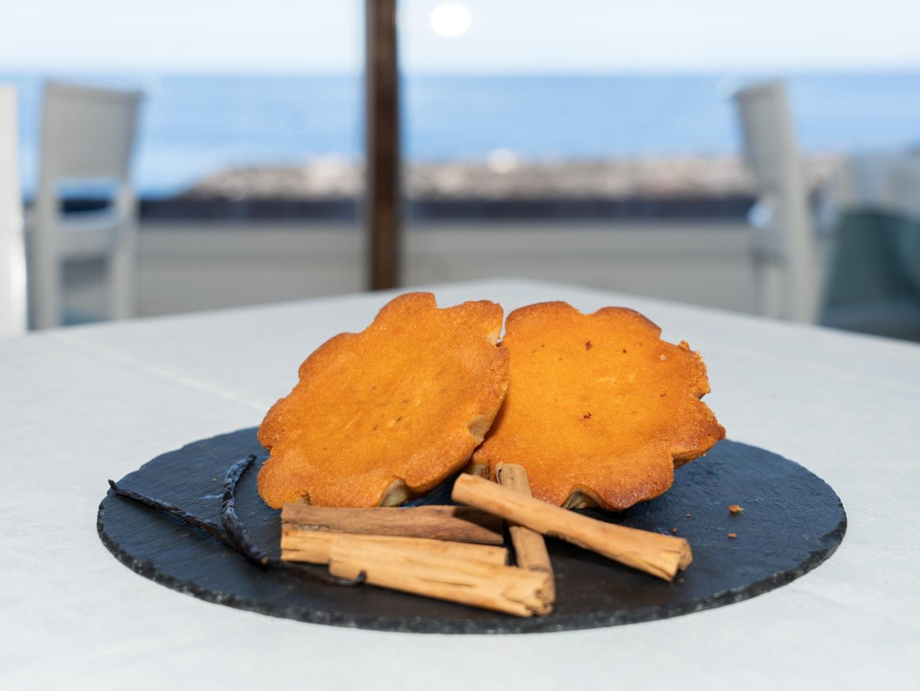 A table with two golden-brown fried items on a slate plate, accompanied by cinnamon sticks.