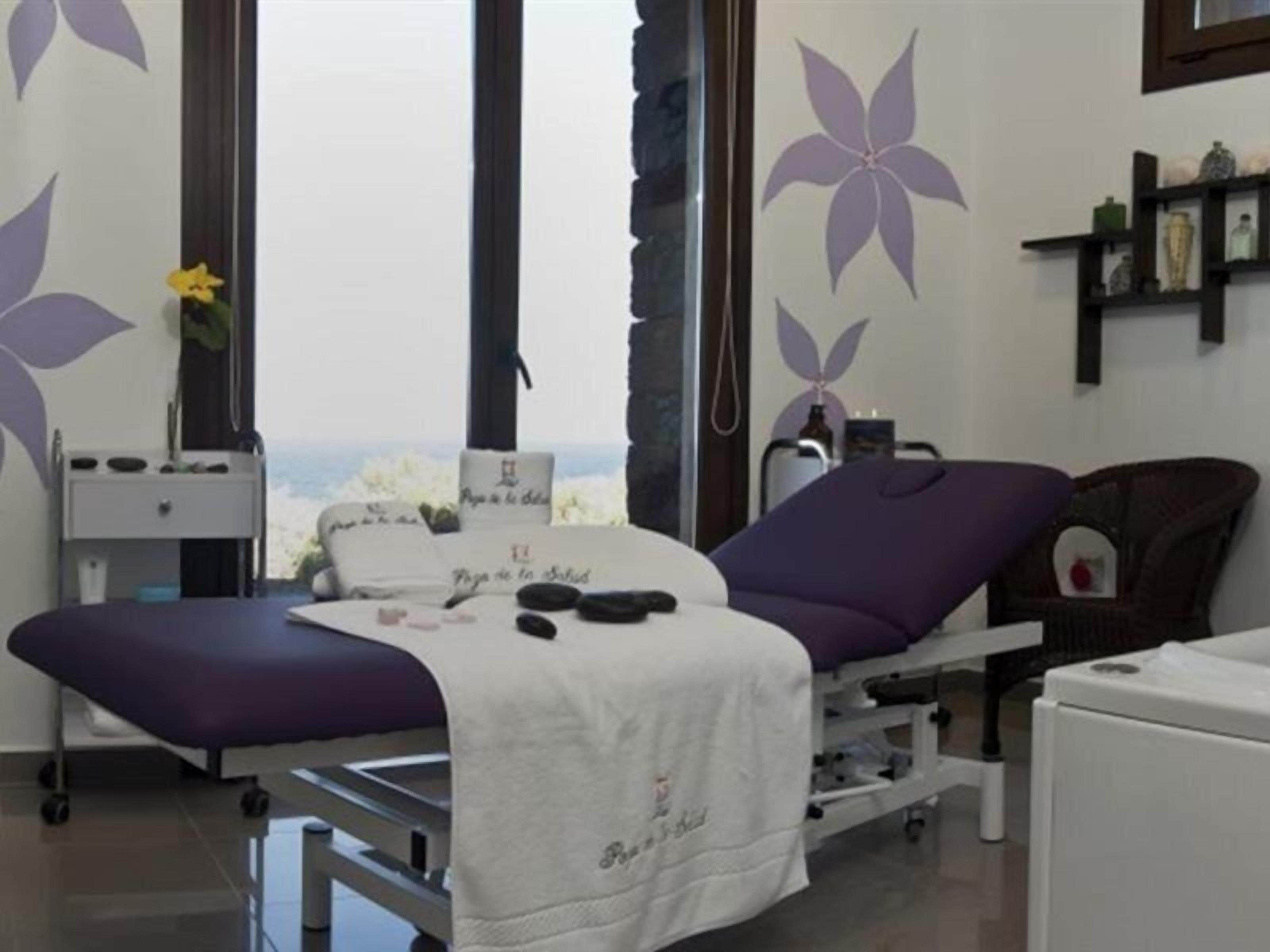 Un consultorio médico con una cama, mesa de exploración y una ventana con vistas.