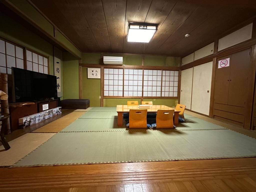 Une pièce de style japonais traditionnel, avec un sol recouvert de tatamis, une petite table basse entourée de coussins et un téléviseur.