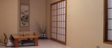 Una habitación con una mesa de comedor de madera, sillas, una planta en maceta, un panel corredero shoji y una obra enmarcada en la pared.
