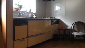 A compact kitchen with a stove, sink, and cabinets. A chair is placed near the sink. - Numazu Ikkyuuan (Numazu)