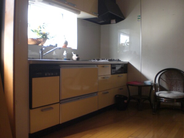 A compact kitchen with a stove, sink, and cabinets. A chair is placed near the sink.