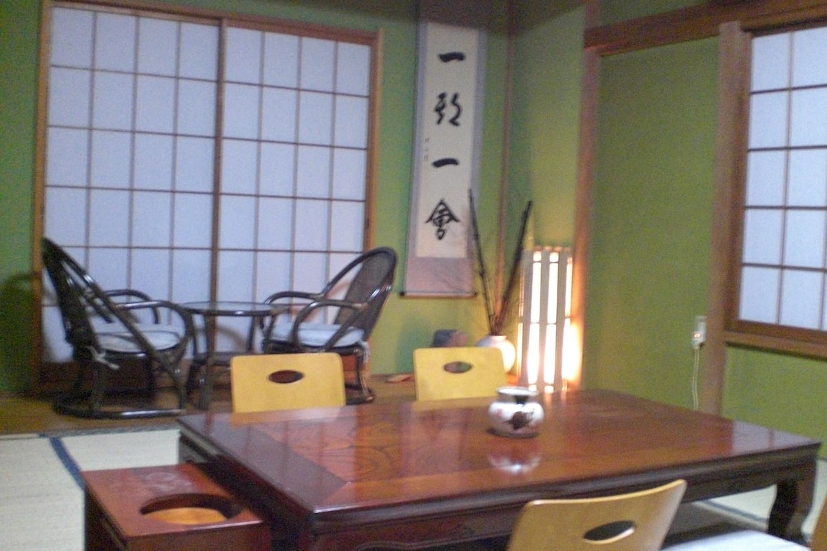 A traditional Japanese dining room with a wooden table, chairs, and a decorative scroll.