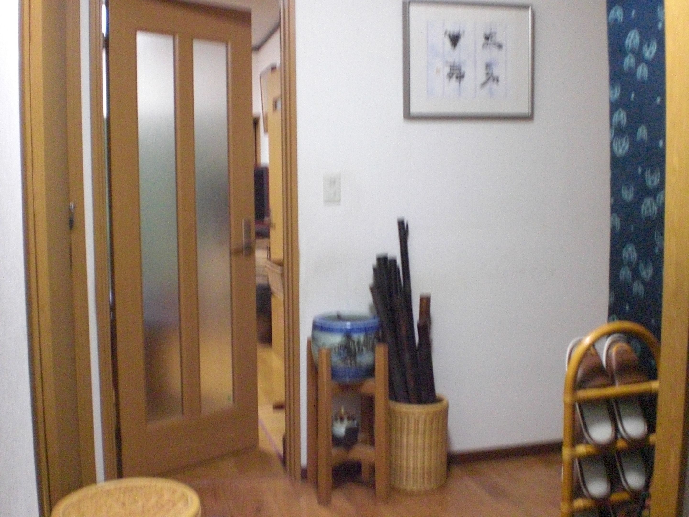 Una habitación con puerta de madera, una mesita con un recipiente azul y una silla de mimbre con estructura metálica.