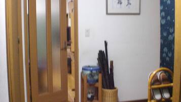Una habitación con puerta de madera, una mesita con un recipiente azul y una silla de mimbre con estructura metálica.