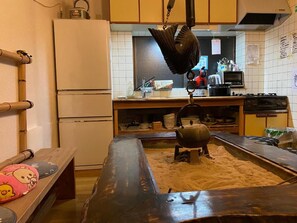A kitchen with a large cooking pot on a stove, a refrigerator, and a wooden bench with cushions. - Numazu Ikkyuuan (Numazu)