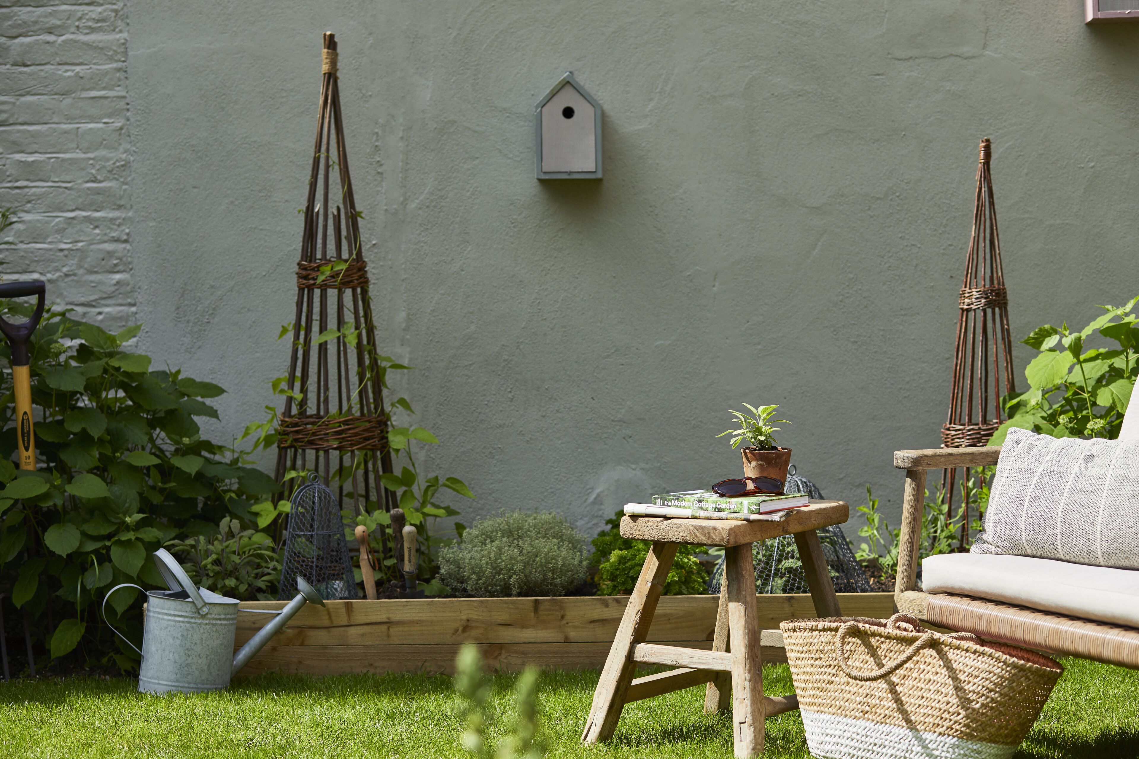 A garden with a wooden bench, a small table with a plant, and a birdhouse on the wall.