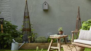 Ein Garten mit einer hölzernen Bank, einem kleinen Tisch mit einer Pflanze und einem Vogelhaus an der Wand.