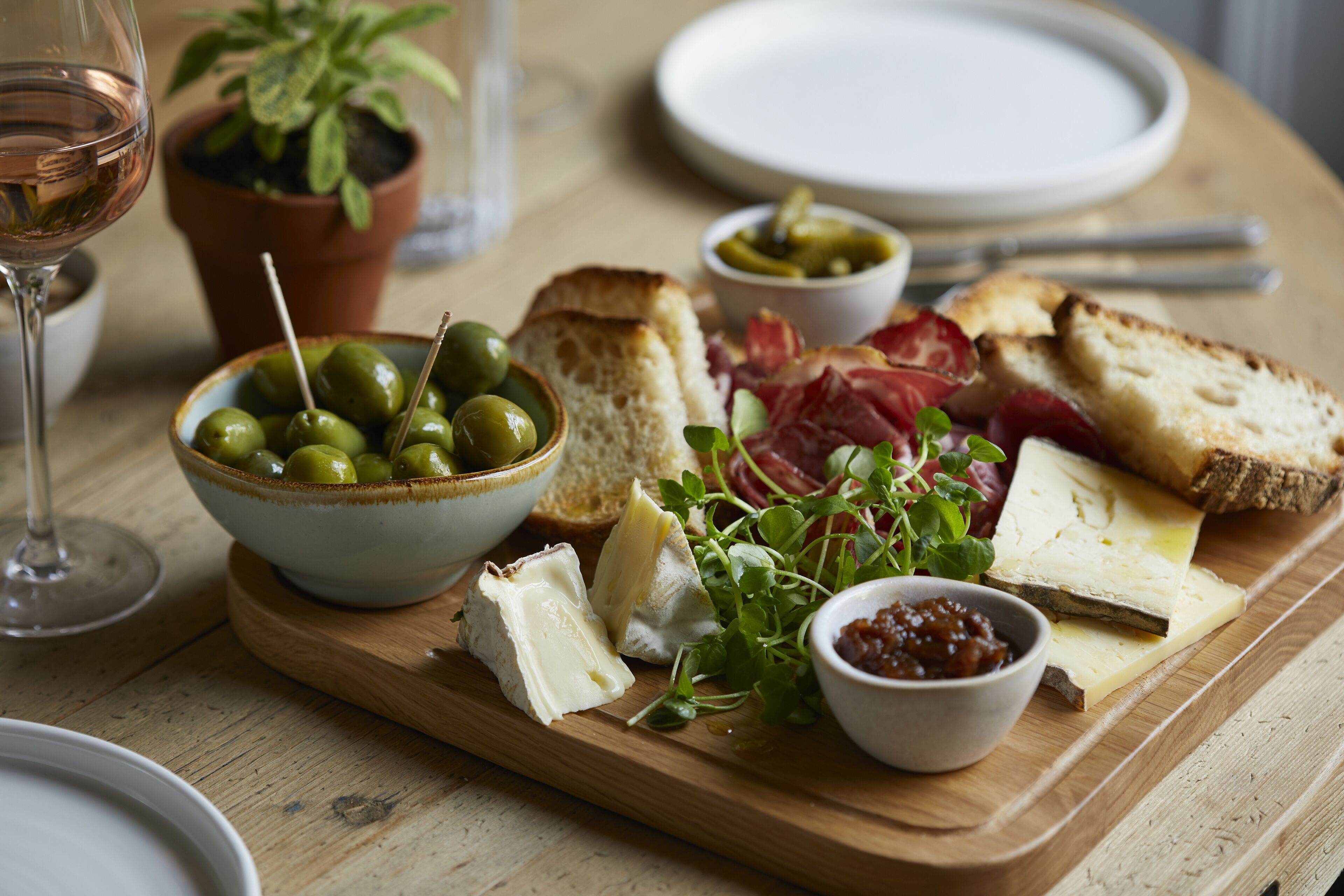 Un tagliere di legno con formaggi assortiti, pane, olive e verdure su un tavolo.